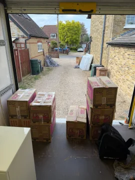 Moving boxes being loaded into an SJC Movers van from a gravel driveway