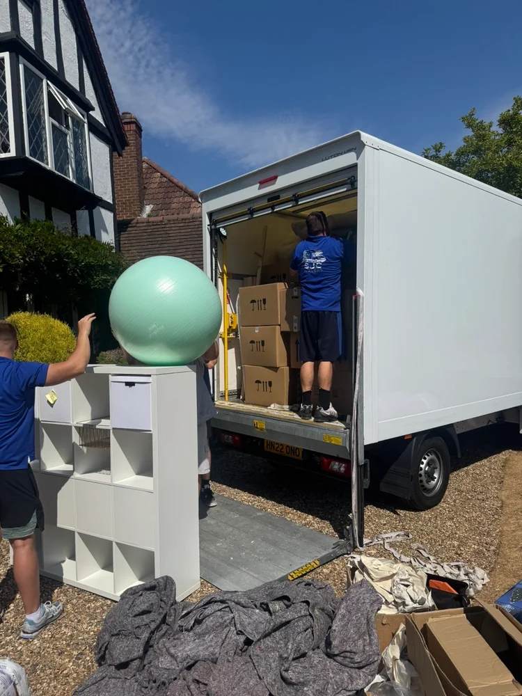 SJC Movers loading a shelving unit and boxes into the van on a gravel driveway